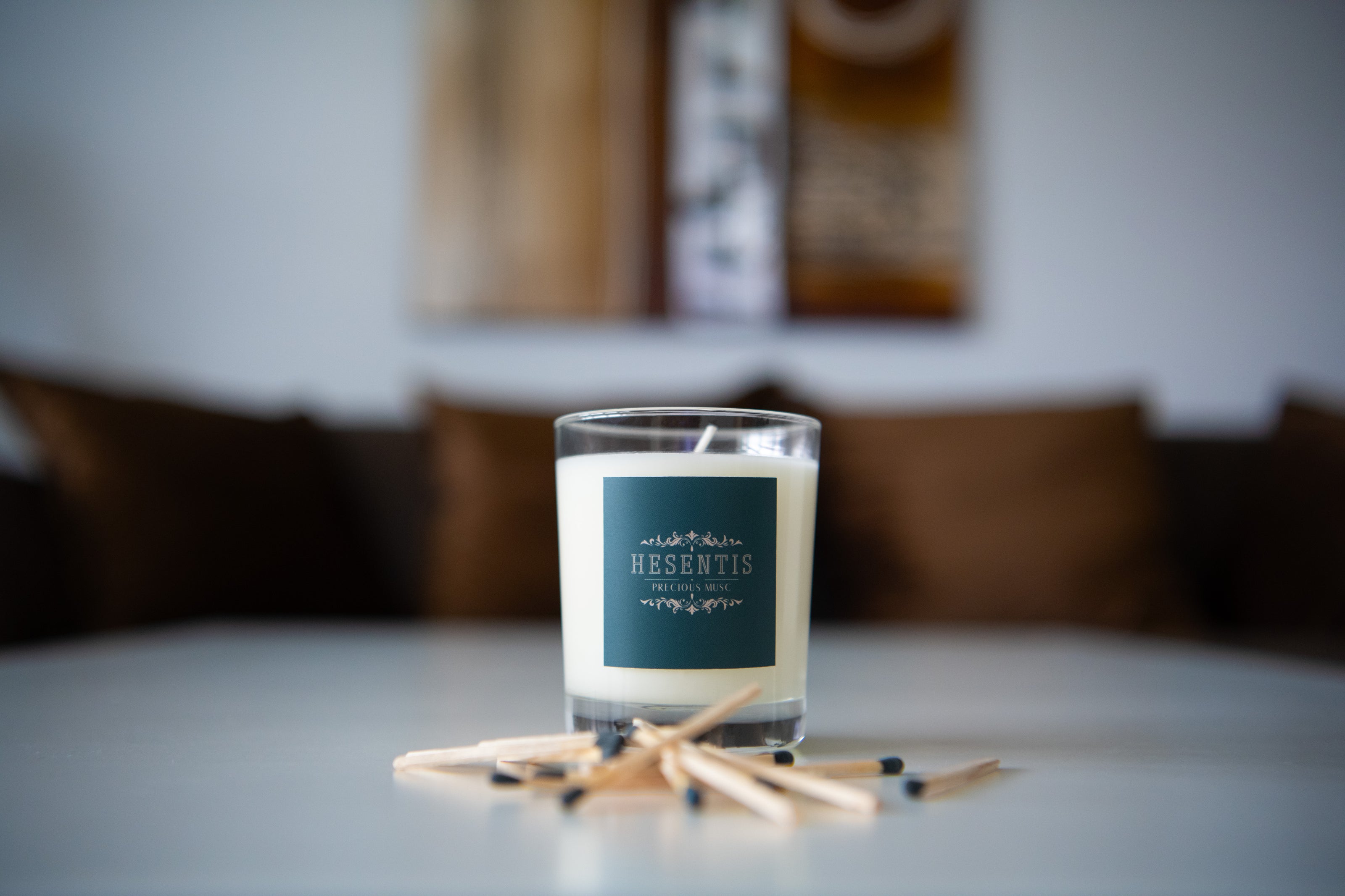 Hesentis scented candle Precious Musc on a stylish table, surrounded by matches, with a warm, cozy interior design in the background.