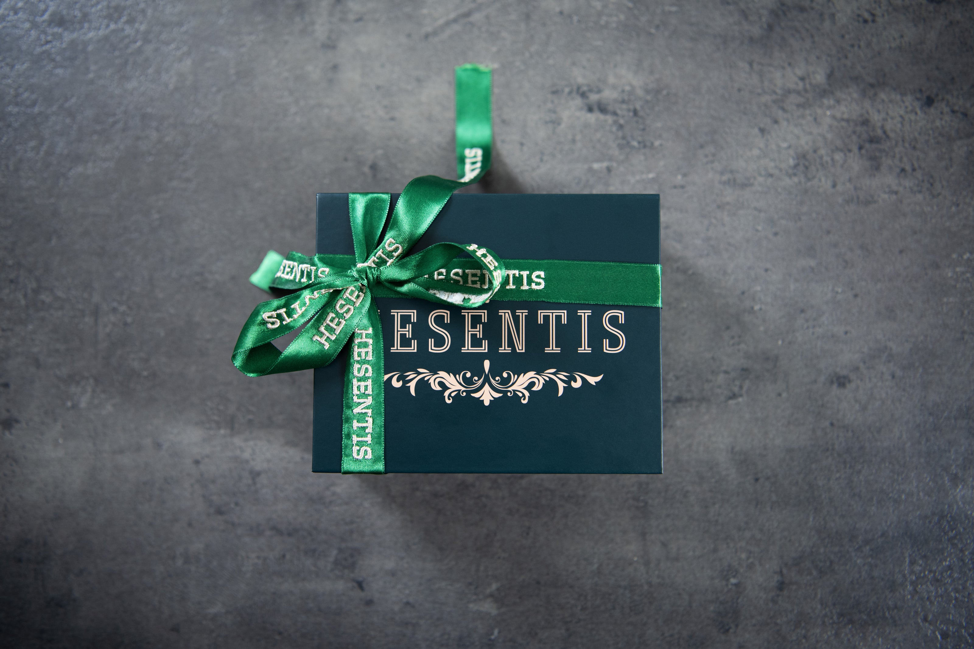 Elegant Hesenits gift box with green bow and gold embossing on a dark background.