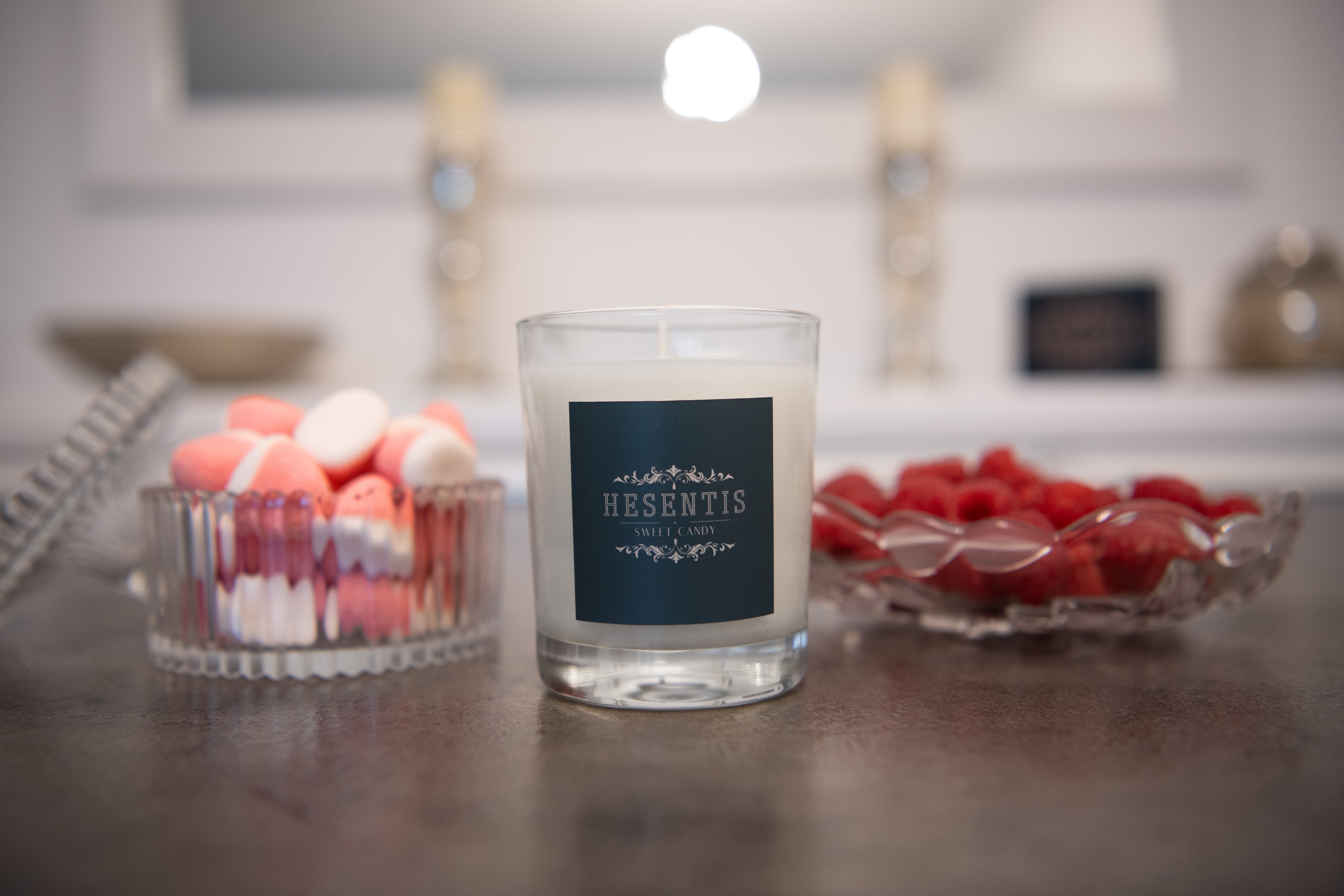 Hesentis Sweet Candy scented candle on a table surrounded by red berries and colorful candies in crystal bowls.